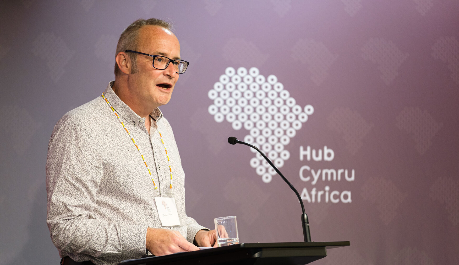 Julian Rosser speaking at the Global Solidarity Summit 2023 with a Hub Cymru Africa logo in the background.